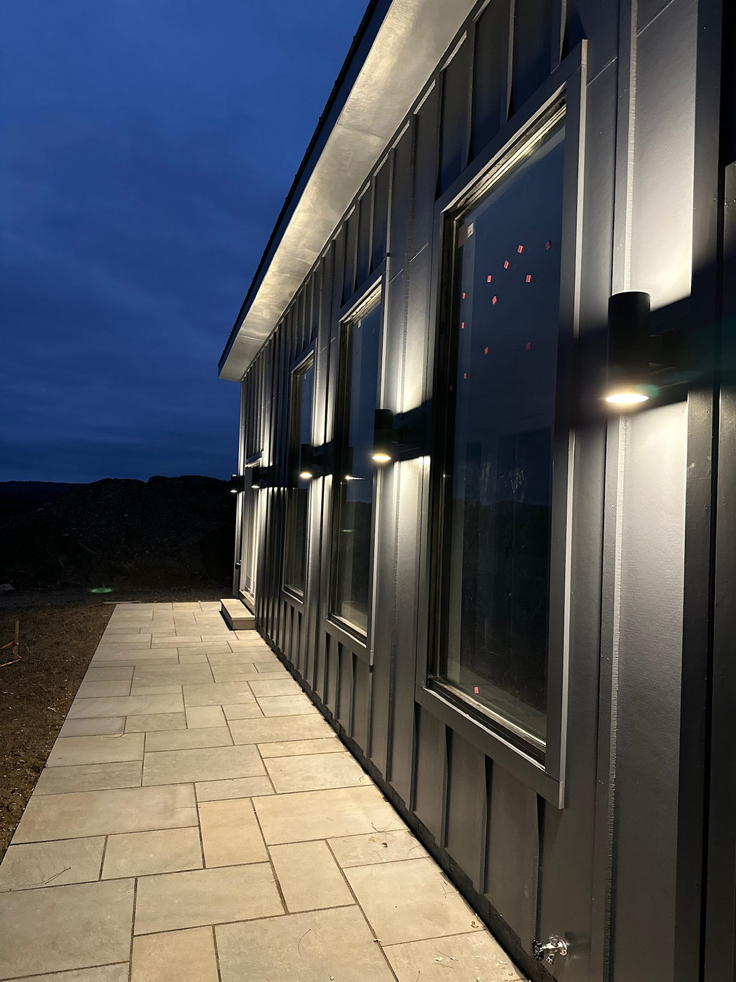 Dark board-and-batten facade lit at dusk beside a bluestone walkway