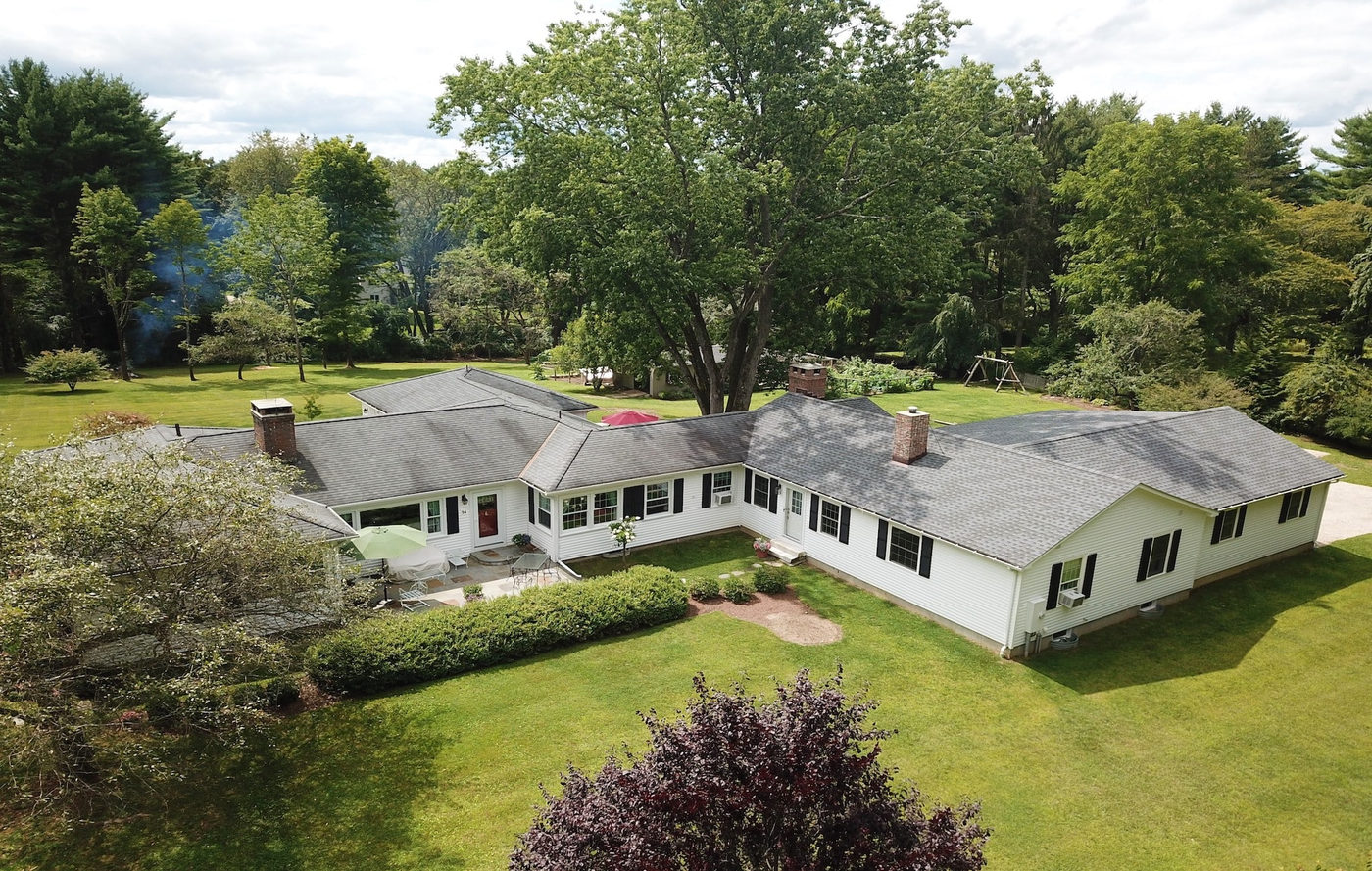 Aerial view of a renovated ranch house surrounded by lawn and mature trees