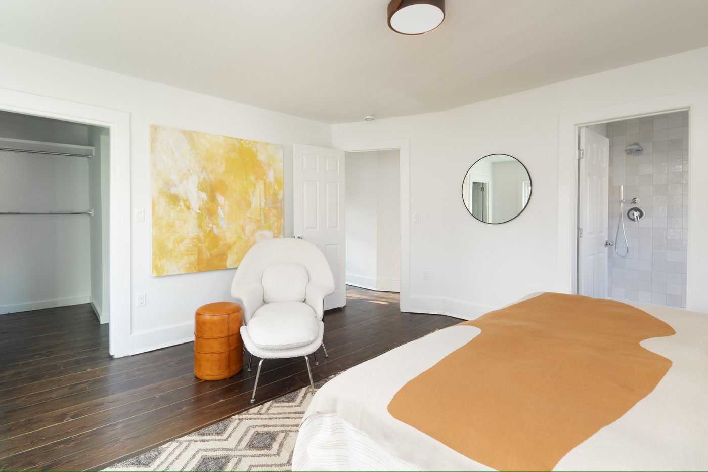 Room with white walls, a round mirror, a white armchair and a soft ochre rug