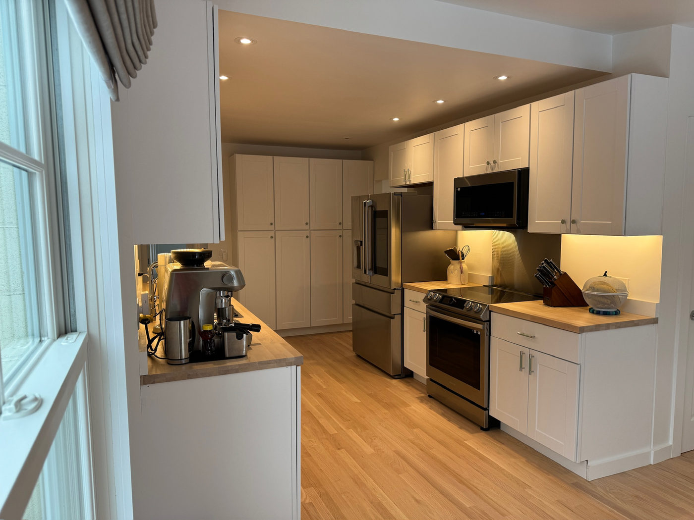 Galley kitchen with white cabinets, stainless appliances and wood floors