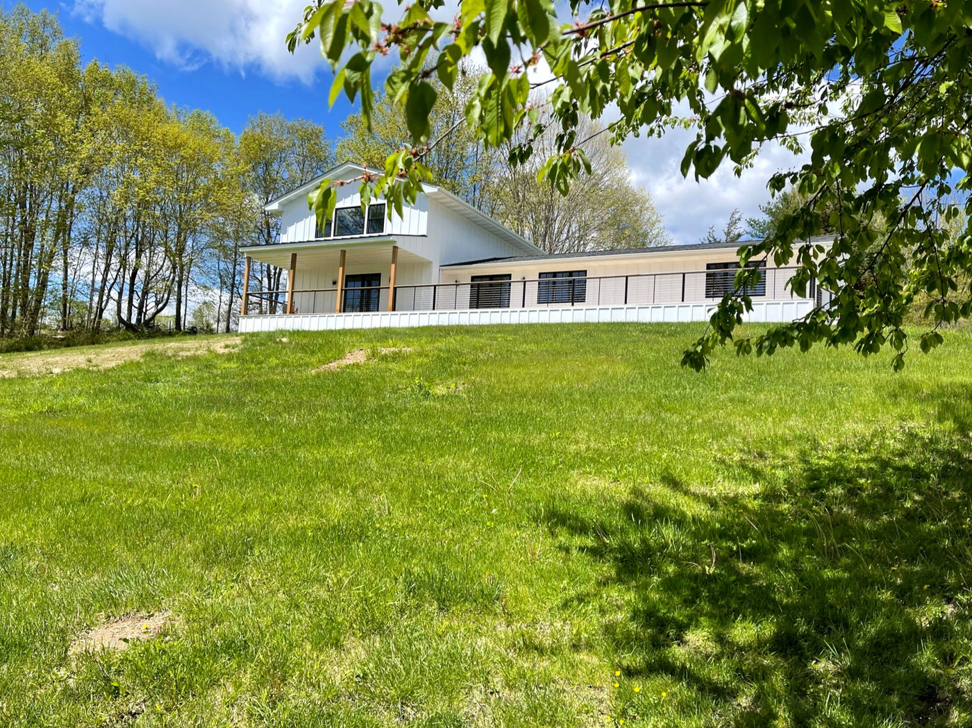 White farmhouse with black windows and a long deck set against wooded hills