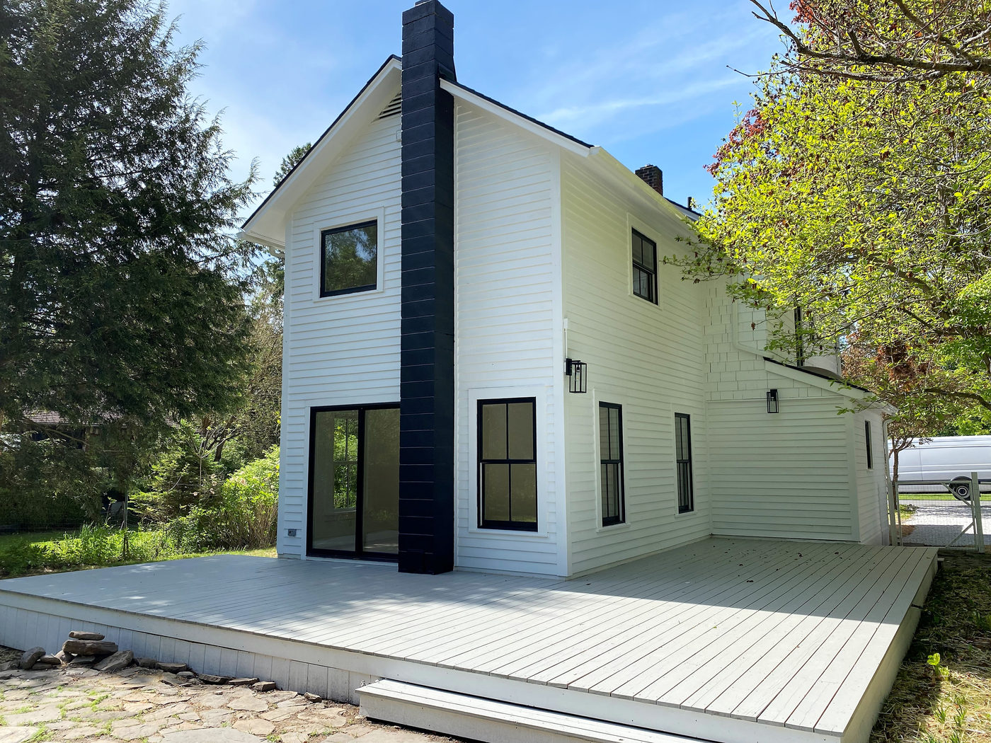 White clapboard house with a black chimney and a new wood deck