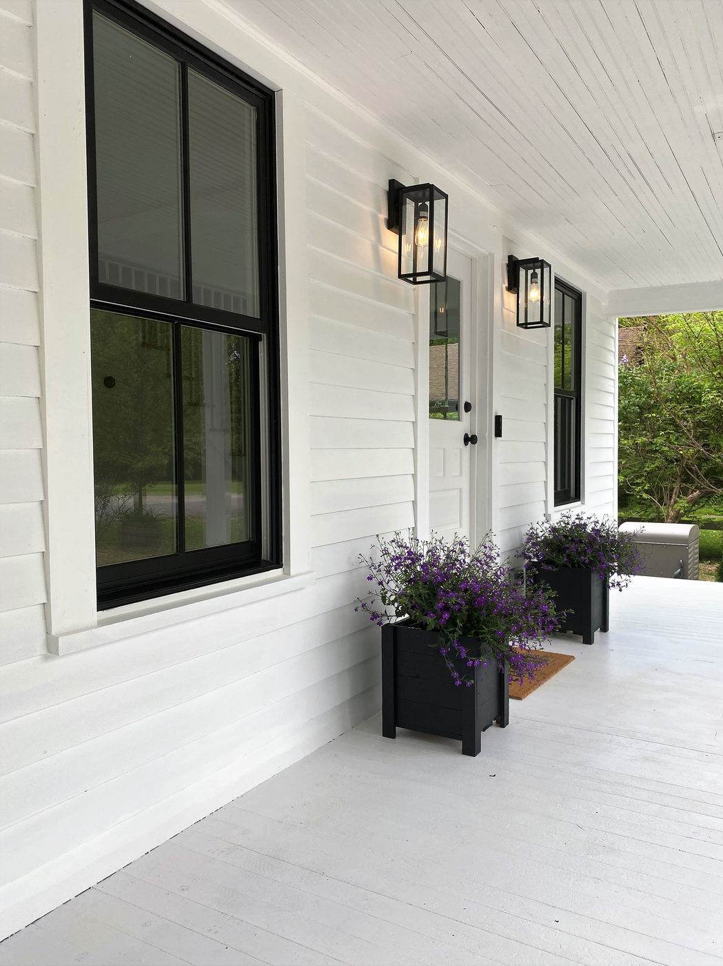 White porch with black-framed windows and planters of lavender