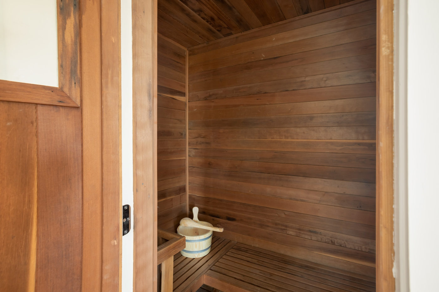 Cedar-lined sauna with a slatted bench and wooden bucket