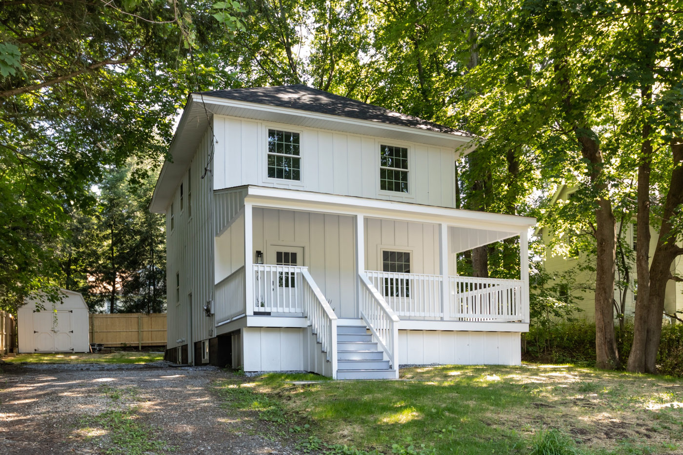 White cottage with a covered front porch under mature trees
