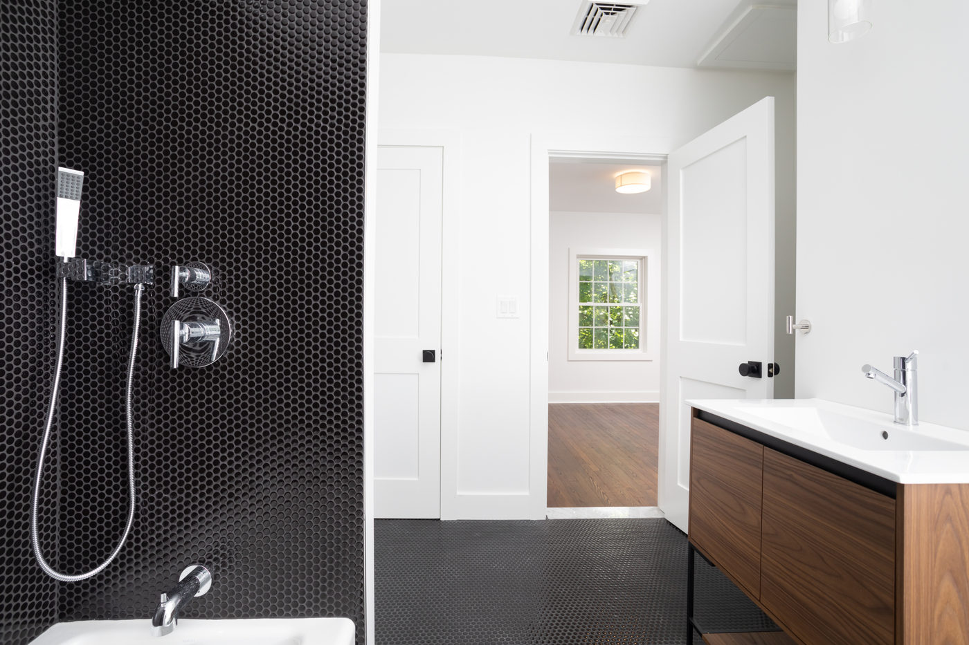 Bathroom with black penny-tile shower, walnut vanity and white walls