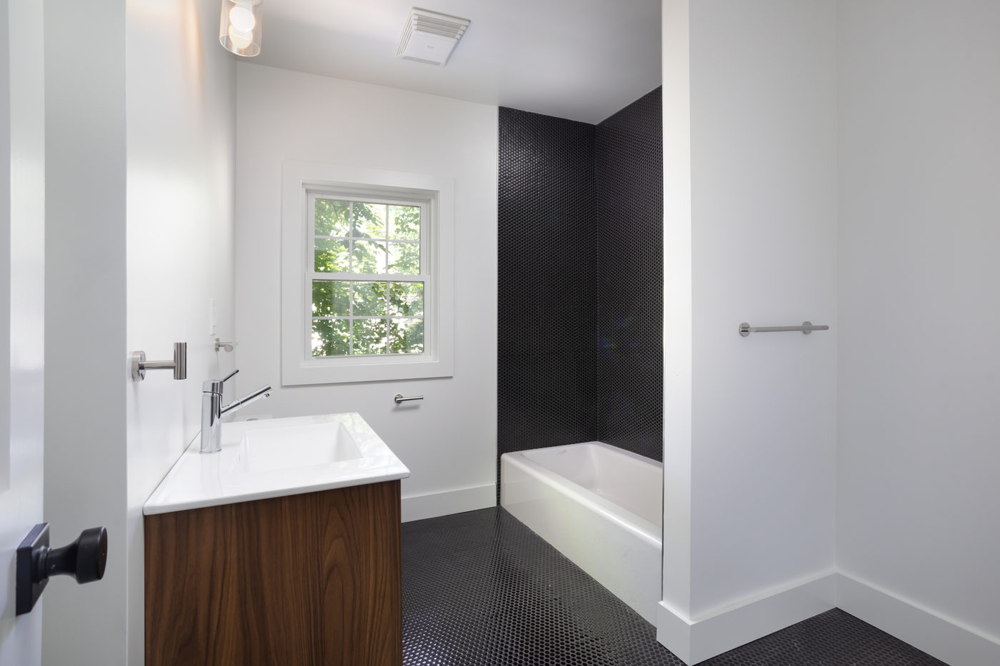 Bathroom with a walnut vanity, white tub and dark tile floor