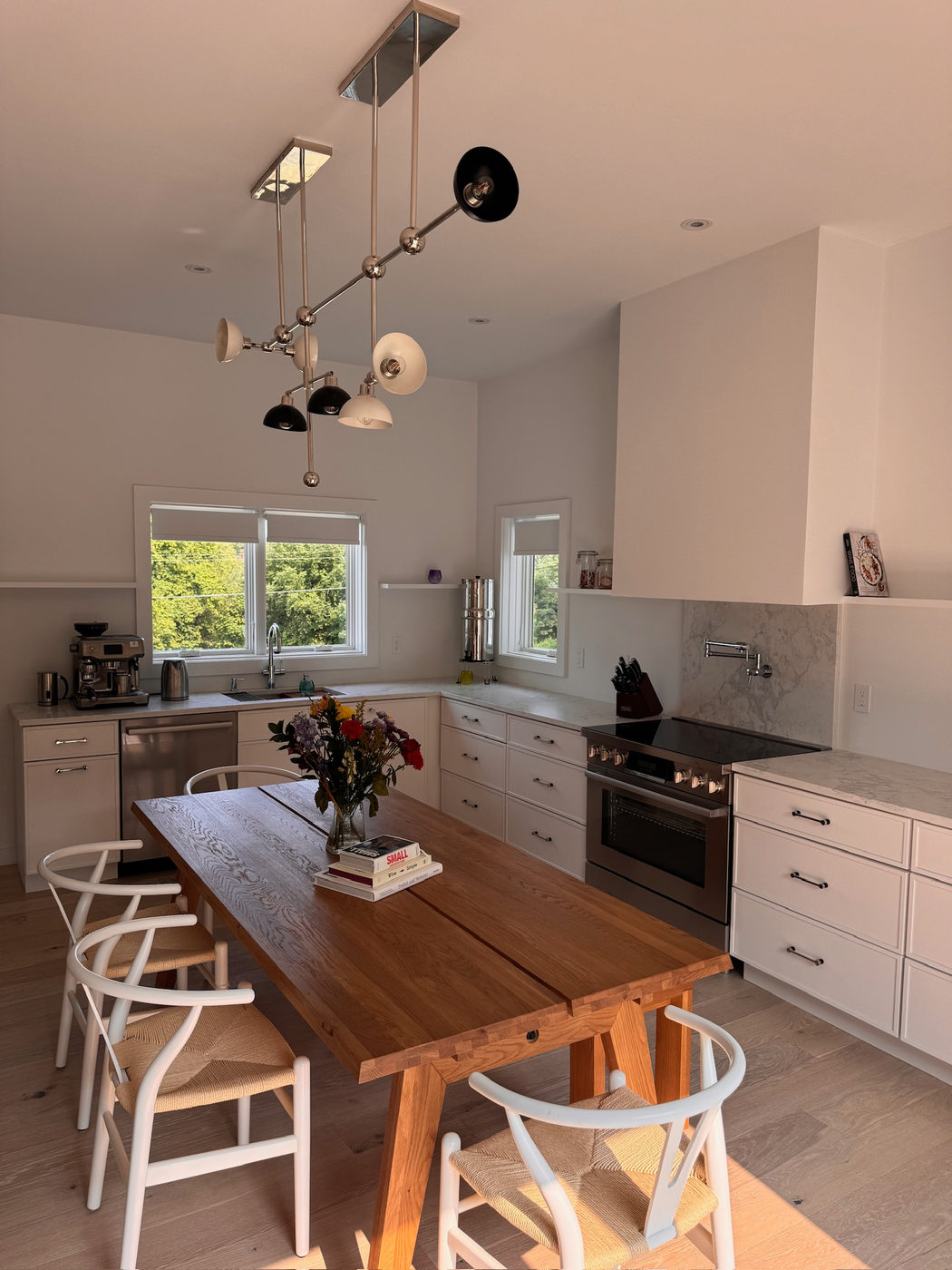 Eat-in kitchen with white cabinets, a wood table and black pendant lights