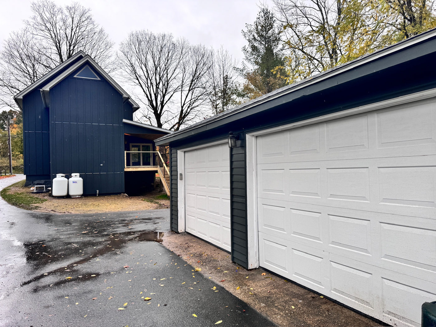 Detached two-bay garage with white doors beside the navy house
