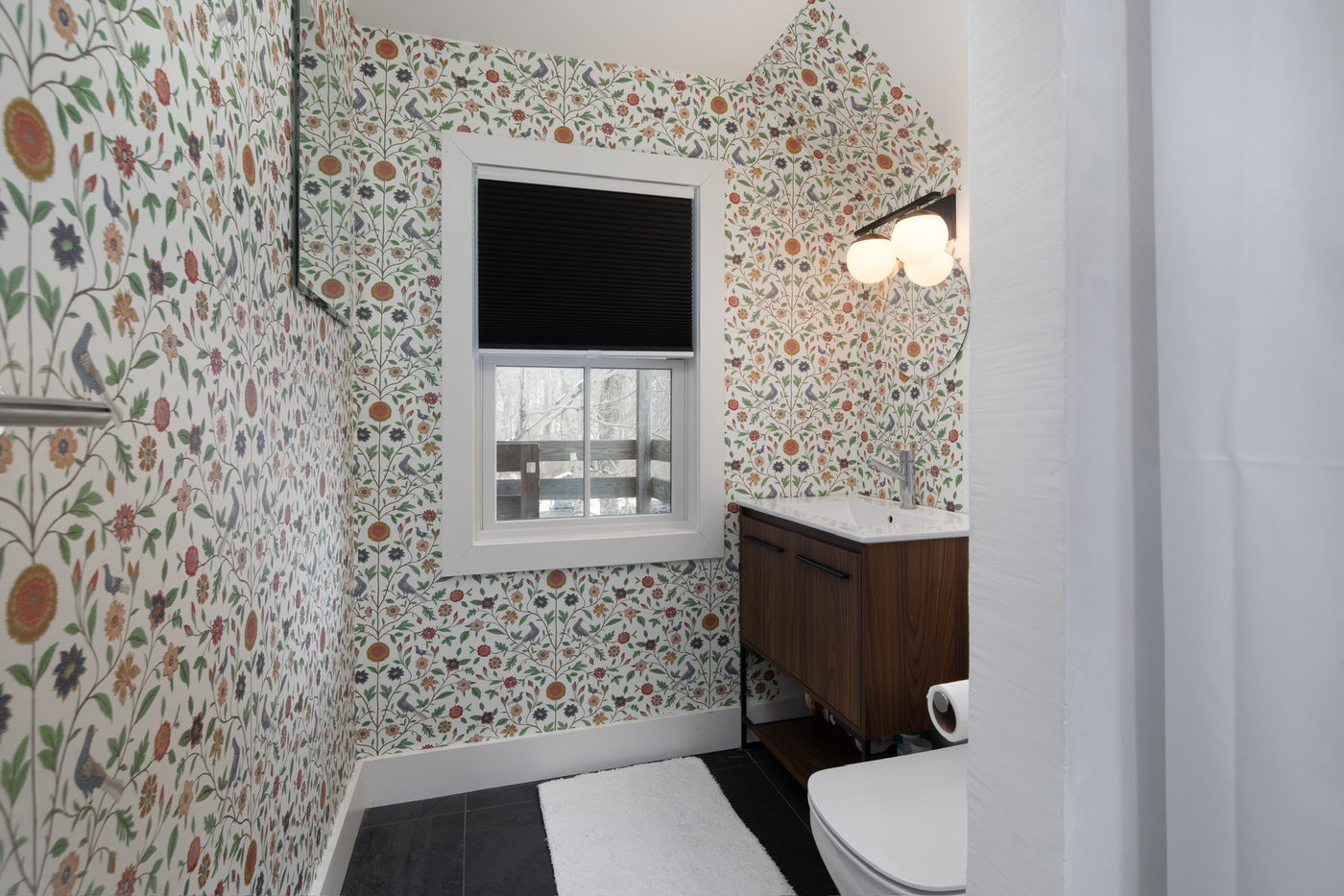 Bathroom with patterned wallpaper, a walnut vanity and a black window