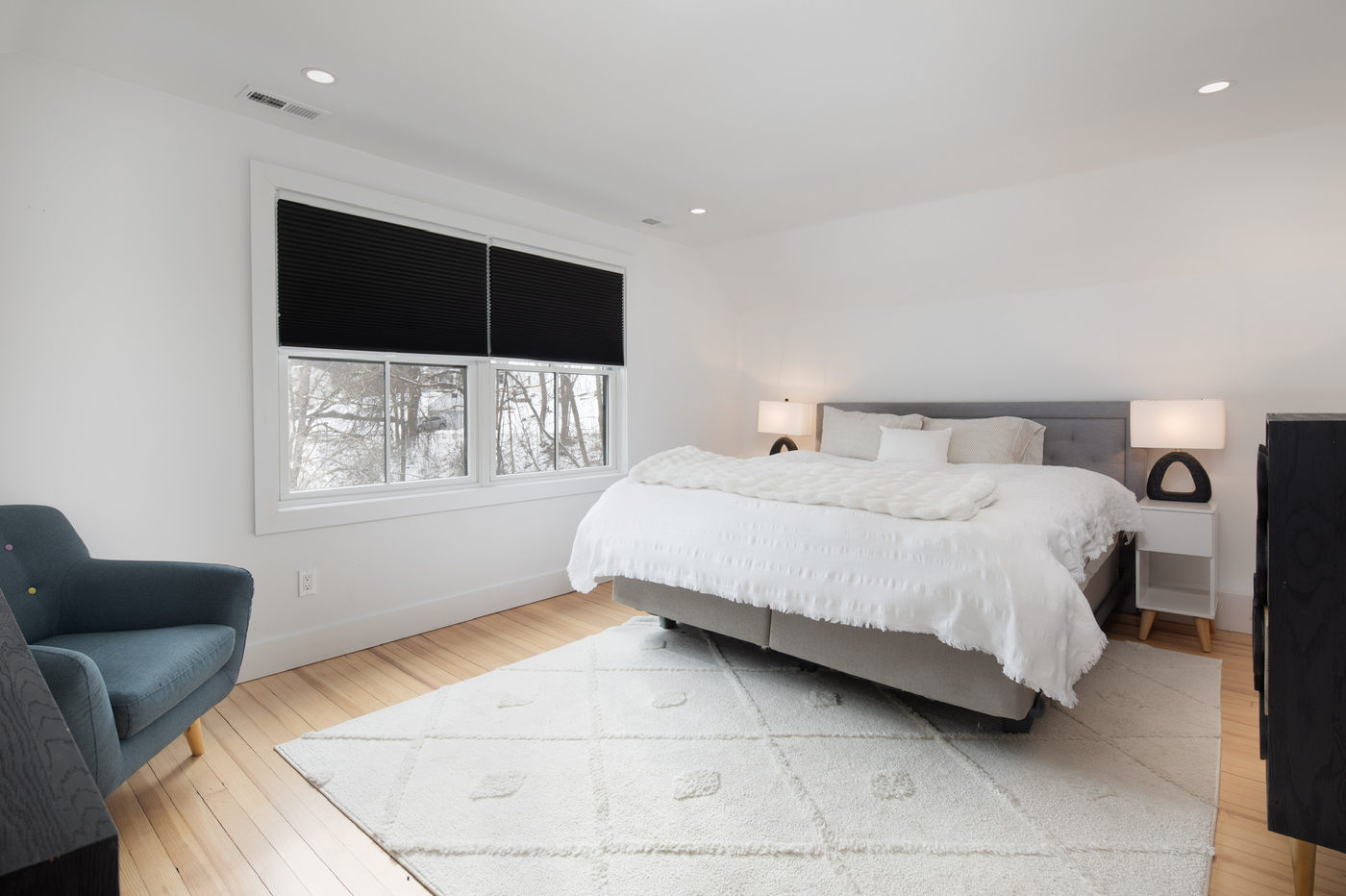 Bedroom with a blue armchair, white bedding and a black roller blind