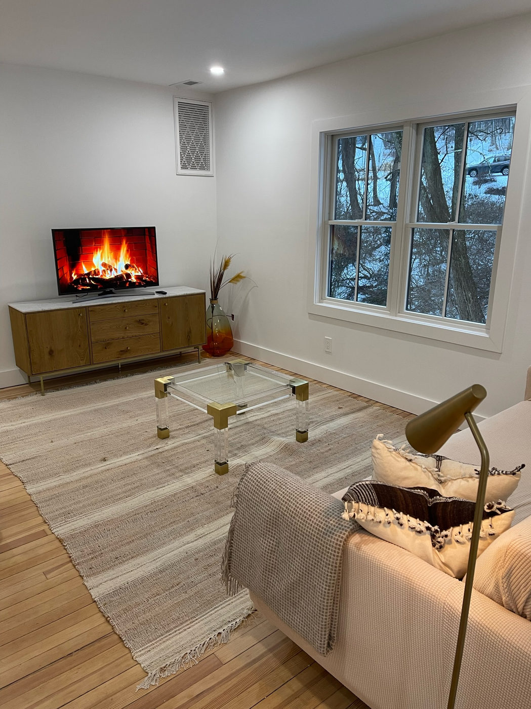 Living room with a sofa, glass coffee table and windows looking into the trees