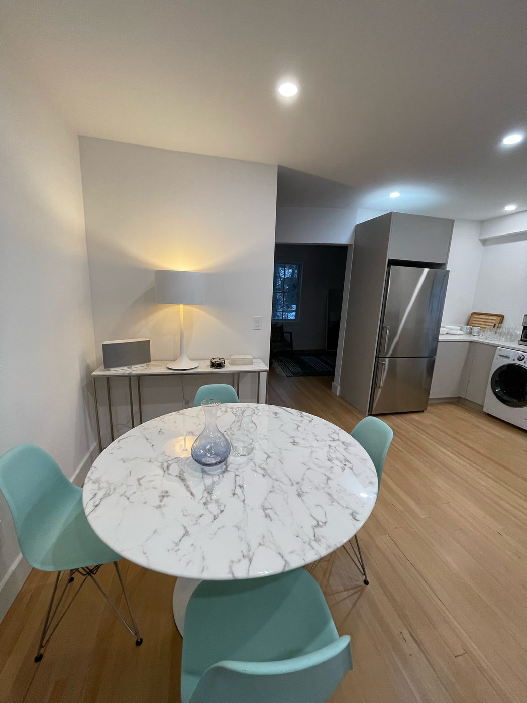 Dining nook with a round marble table and teal chairs, kitchen and laundry beyond
