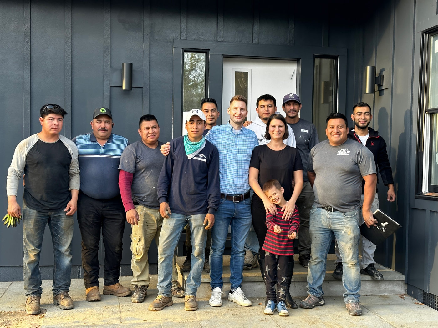 The EJ Home crew standing together in front of a dark board-and-batten house